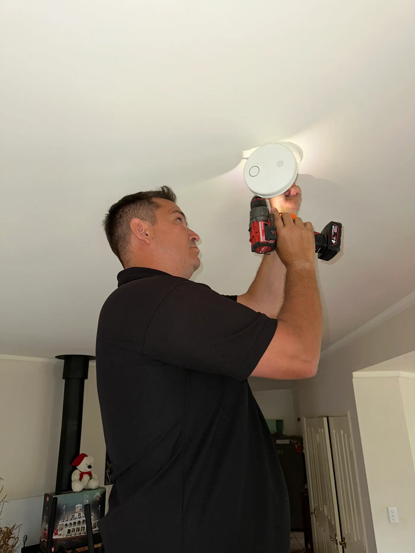 Licensed Spanos ElectriCool technician servicing a smoke alarm in Brisbane